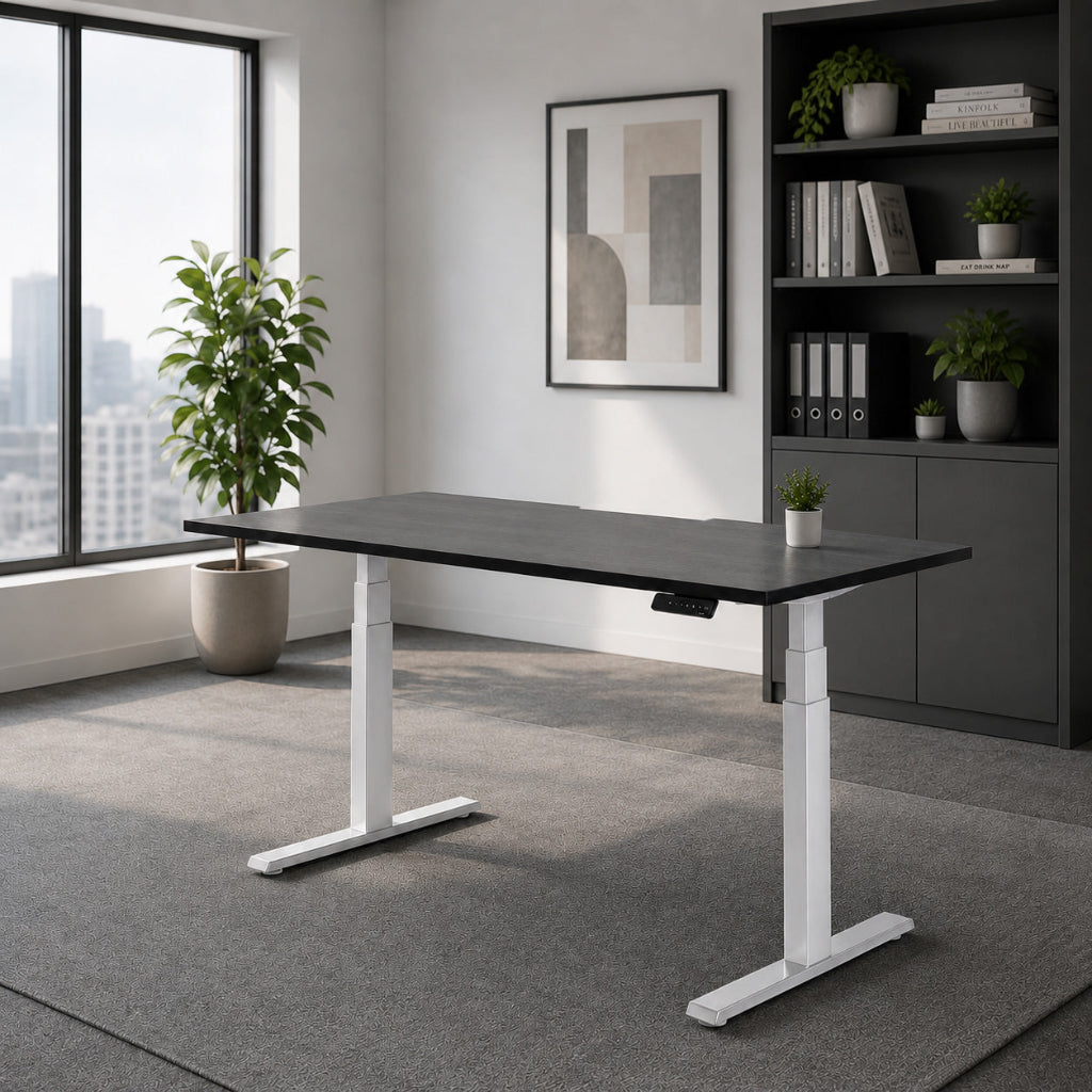 A modern standing desk with a black top and white T-style legs, placed in a bright, contemporary home office with a gray carpet, a window view, and a dark gray shelving unit in the background.
