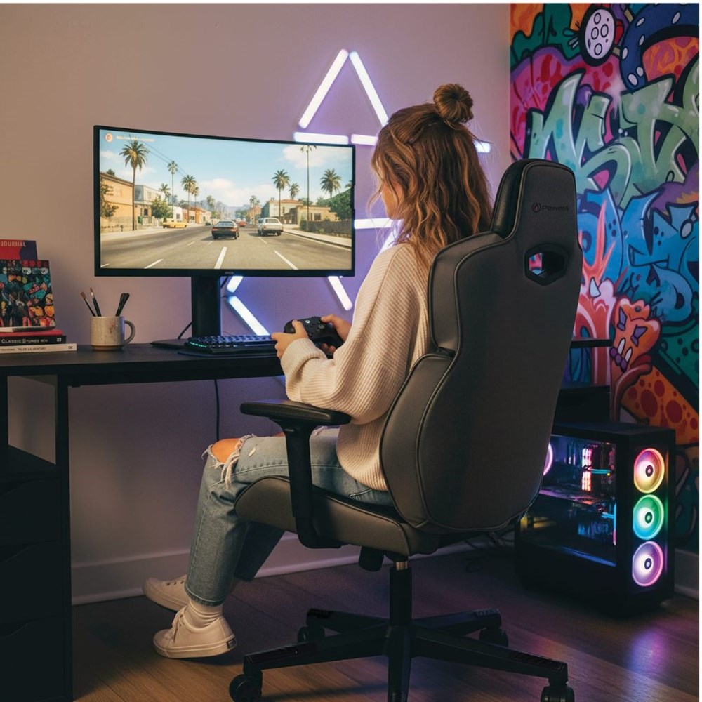 Person playing a racing game on a computer in a colorful room with gaming setup.