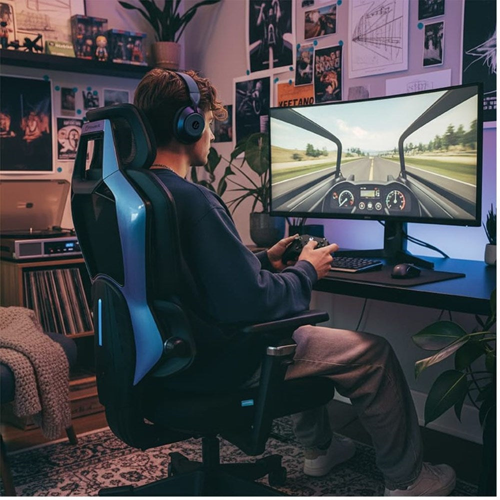 Person playing a racing game on a computer in a room with gaming setup and posters.