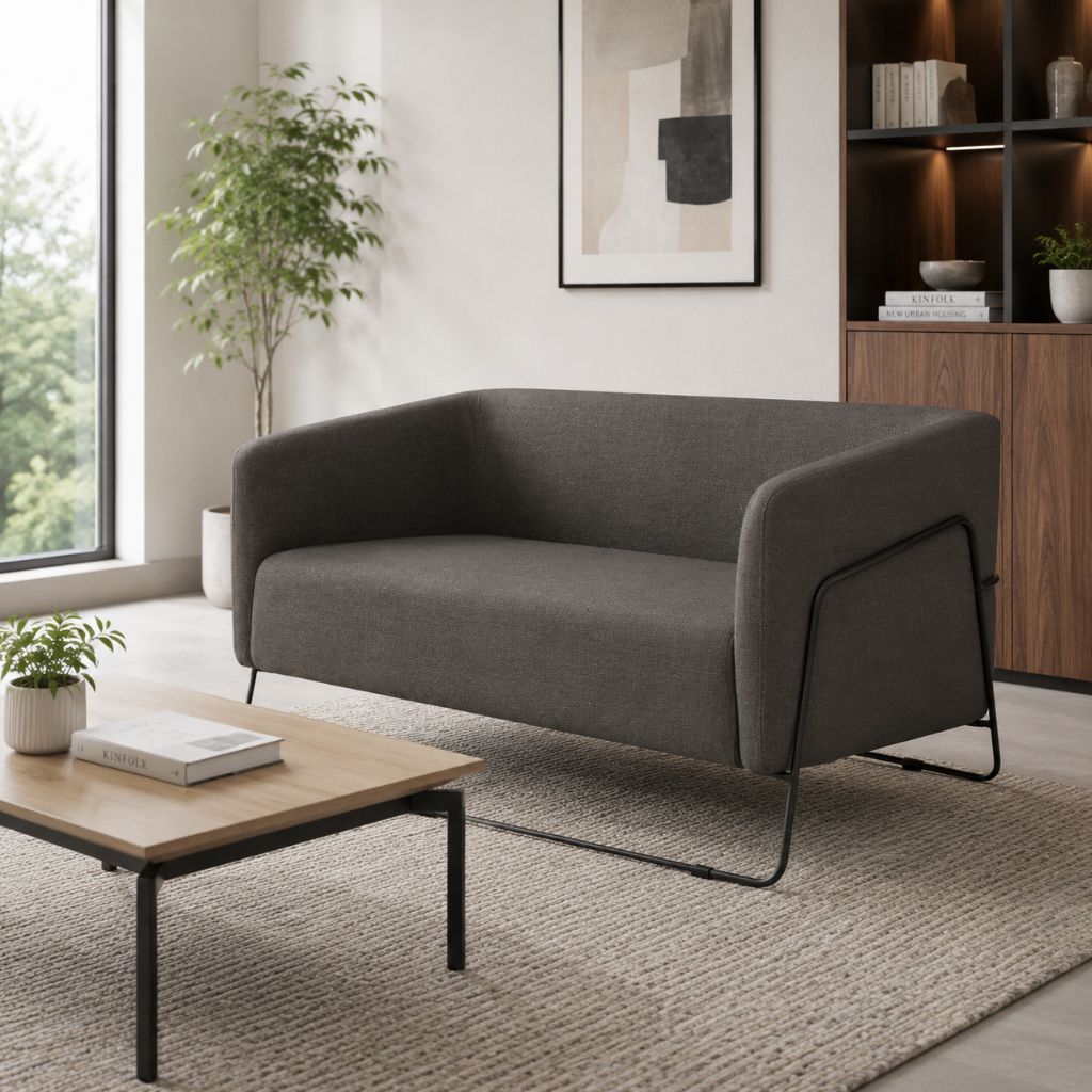 A modern two-seater sofa in dark gray fabric with black metal legs, styled in a bright, contemporary living room next to a wooden coffee table and a textured rug.