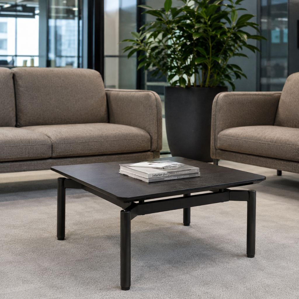 A modern square coffee table with a dark wood top and black metal legs, styled in a contemporary living room setting with a beige sofa and armchair in the background.