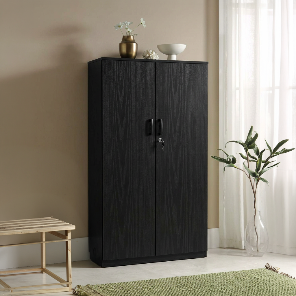 A tall black wood-grain cabinet with two doors and a lock, styled in a room setting next to a window with sheer curtains, a small wooden bench, and a green rug.